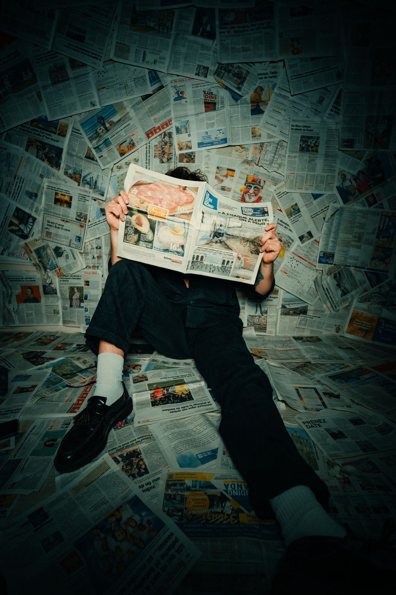 A reader behind a newspaper, surrounded by front pages