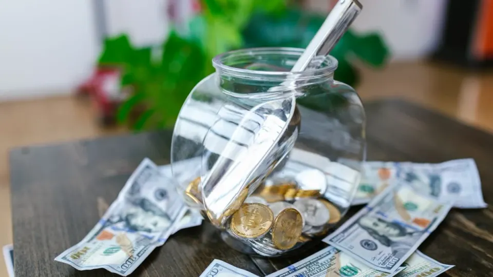 A jar of coins next to dollar banknotes